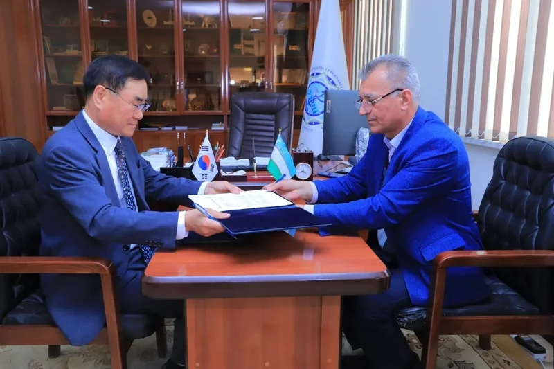 Two seated participants hold an open blue agreement folder across a wooden table
