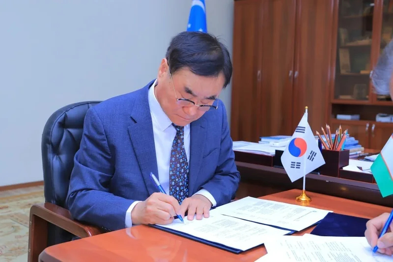 A participant signs a document beside South Korean and Uzbek desk flags